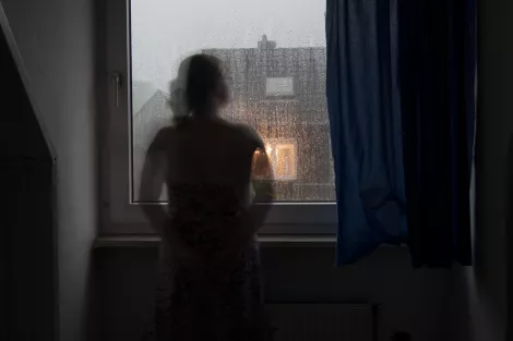 A lady standing in front of the window during a rainy day A lady standing in front of the window during a rainy day